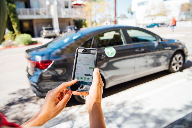 a person holds a phone to look at an app in front of a rentable car